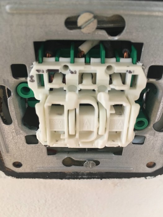 Närbild på en osammanfogad eluttag under installation mot en vit vägg.