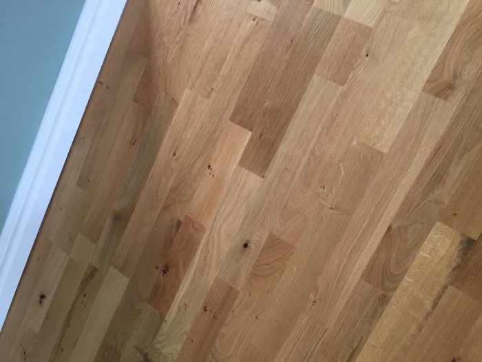 Närbild av nytt parkettgolv med vita prickar, några med svart i mitten, vid list och tom yta.