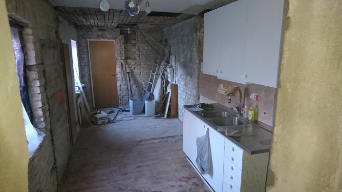 Orenoverat kök under renovering med synliga tegelväggar, köksskåp och renoveringsmaterial utspridda.