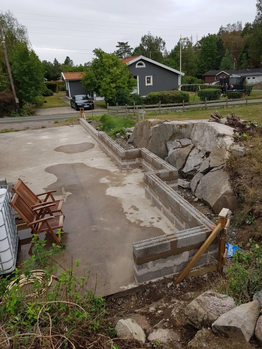 Grundläggande murbyggnadsarbete utanför hus, med oputsade block och konstruktionsmaterial.