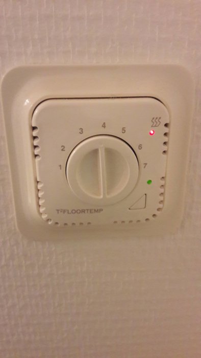 Vit termostat för golvvärme T2FloorTemp med röd och grön lampa tänd och inställningsratten vriden.