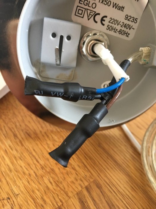 Vägglampa med oskyddade, ej inkopplade elsladdar nära en strömbrytare, installationsvarningsetikett synlig.