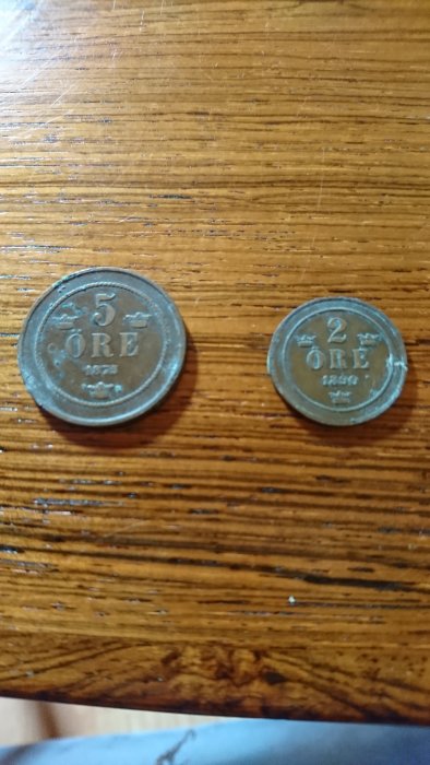 Två gamla svenska mynt på en träyta; en 5 öres mynt från 1874 och en 2 öres från 1890, vilket tyder på husets ålder.