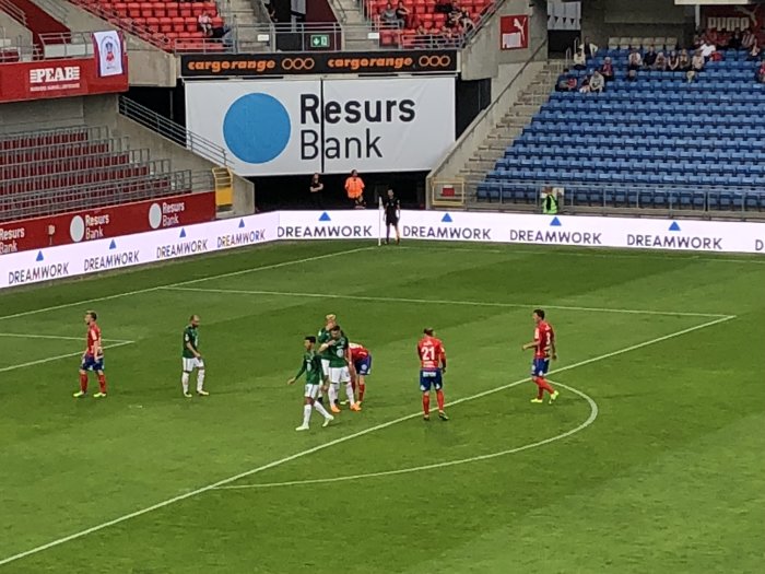 Fotbollsspelare på plan under en live match med LED-reklam i bakgrunden.