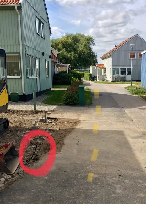 Gata med pågående schaktarbete och en markerad uppstickande slangstump för fiber vid ett hus.