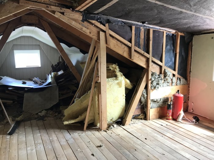 Interiör av vind med original takstolar och ersatt sned stötta, isolering och bråte.
