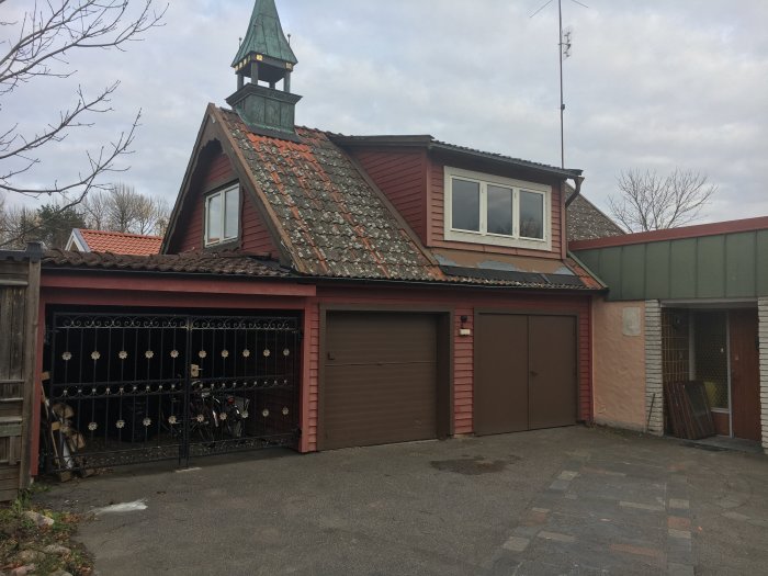 Hus med rött tegeltak och garagedörrar innan renovering, ovanpå garage vitmålat rum med fönster.