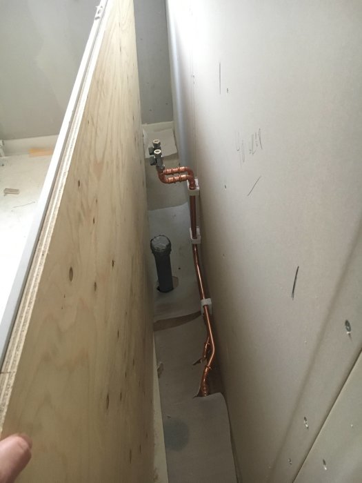 Rörmokararbete med kopparledningar och ventiler installerade nära en plywoodvägg och ljusgrå gipsskivor.