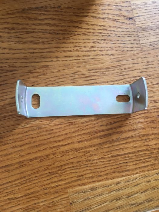 Metallskena tänkt att fästas i väggen för montering av lampfot, ligger på ett träbord.