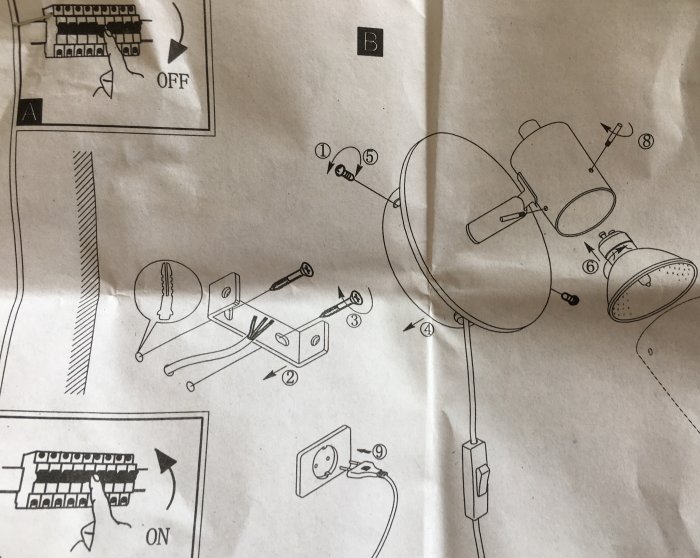 Monteringsanvisning för vägglampa visar detaljerade delar och monteringssteg på en pappersmanual.