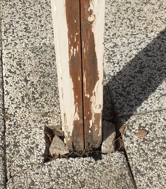 En vitmålad trästolpe som murknar vid basen nära marken på en stenlagd yta.