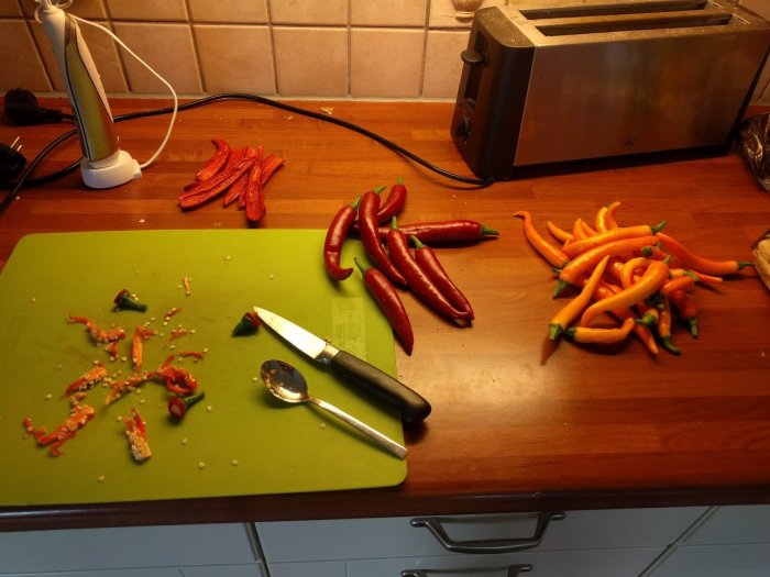 Skuren röd och orange chili på en skärbräda och träköksbänk med en sked och knivar.