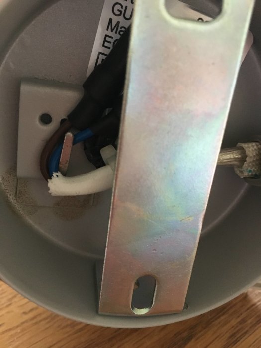 Eluttagets insida med blå och brun sladd fästad i klämma och en närliggande metallplatta.