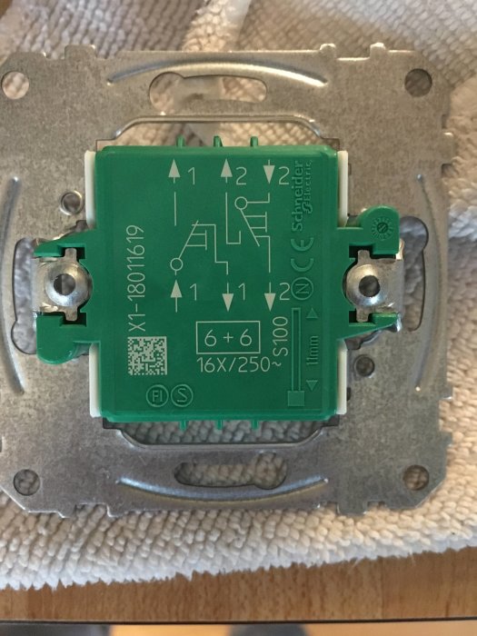 Elektrisk kopplingsdosa i grönt med tekniska diagram och specifikationer, monterad på en grå metallplatta.