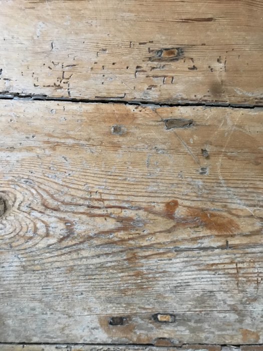 Närbild på gammalt obehandlat plankgolv med synliga spikar och slitagetextur.