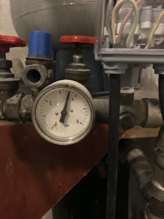 Manometer som visar ungefär 1 bar tryck med rörledningar och ventiler i bakgrunden.