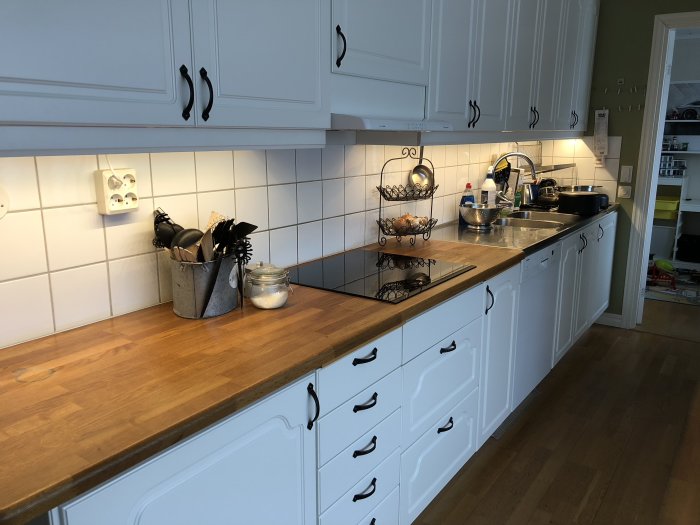 Ett kök med vit inredning och träarbetsbänk belyst av Philips Hue Lightstrips under skåpen.