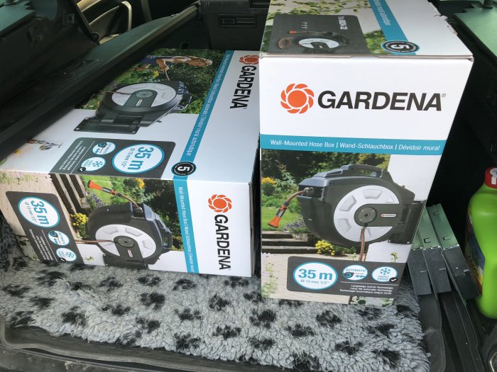 Gardena slangvindor i förpackningar staplade i bagageutrymme, köpta för huset i grå färg.