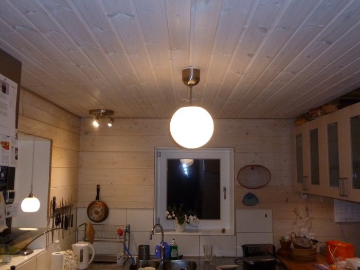 Kök utan överskåp med en armatur av tre spotlights i taket, vitmålade väggar och träpanel.