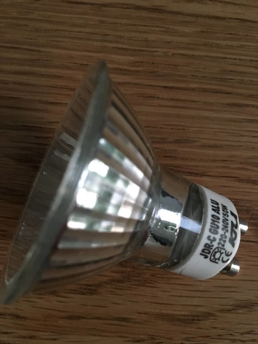 Närbild på en halogenlampa med etiketten JDR 50W visande kopplingsdetaljer mot träbakgrund.