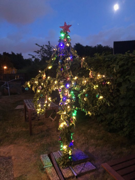 En modern midsommarstång dekorerad med färgglada ljusslingor i kvällsbelysning utomhus.