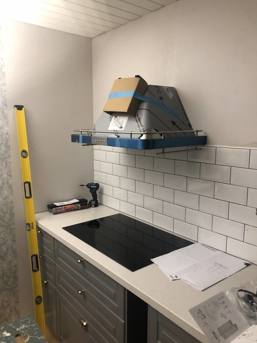 Kök under renovering med kaklade väggar, omonterad köksfläkt och verktyg på bänkskiva.