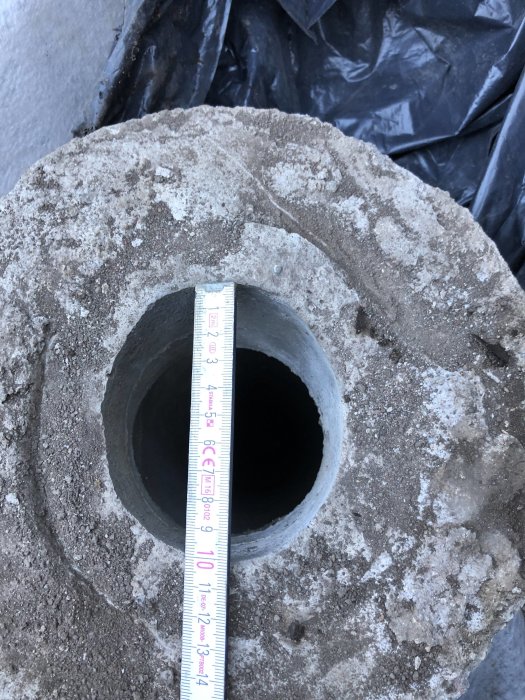 Måttband som mäter diametern på ett avgrävt betongrör i marken, potentiell del av ett avloppssystem.