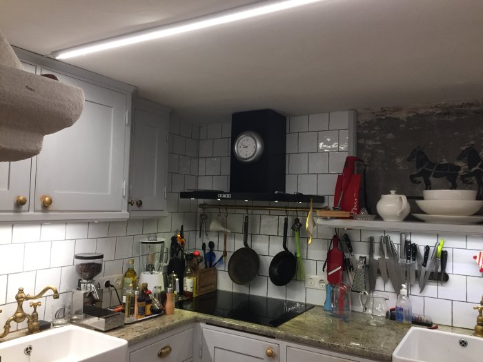 Kök med LED-stripbelysning i tak och under skåp, spotlight under köksfläkt och diverse köksredskap.