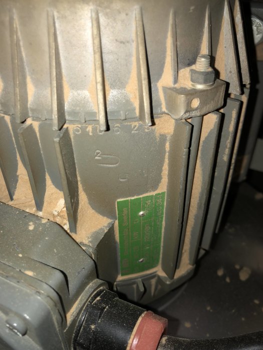 Närbild på en elmotors märkplåt och delar av motorhuset med otydliga rotationsangivelser.