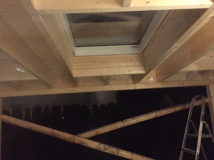 Installation av tunga takfönster i ett träbjälklag under konstruktion, med synligt regelverk och en stege.