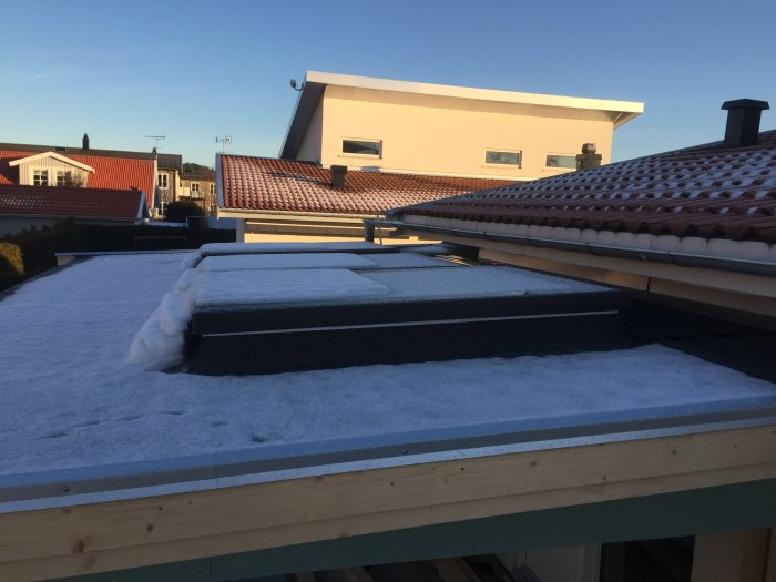 Nybyggt uterumstak med snötäckt takfönster, intill äldre tak med fösta snön som fallit.