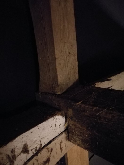 Närbild på en träkonstruktion med mörka fläckar och damm i en byggnad.