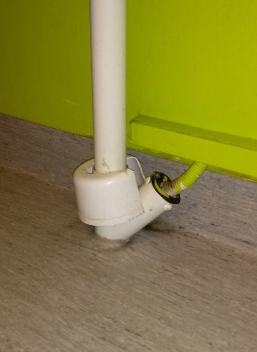 Vit rördel med skadad gul kabel som sticker ut nära golv och vägg.