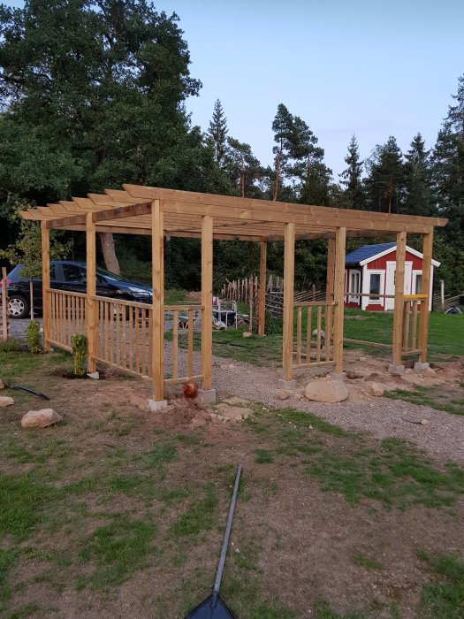 En nybyggd träpergola med stolpar och delvis pålagt tak utan grindar, belägen utanför ett hus.