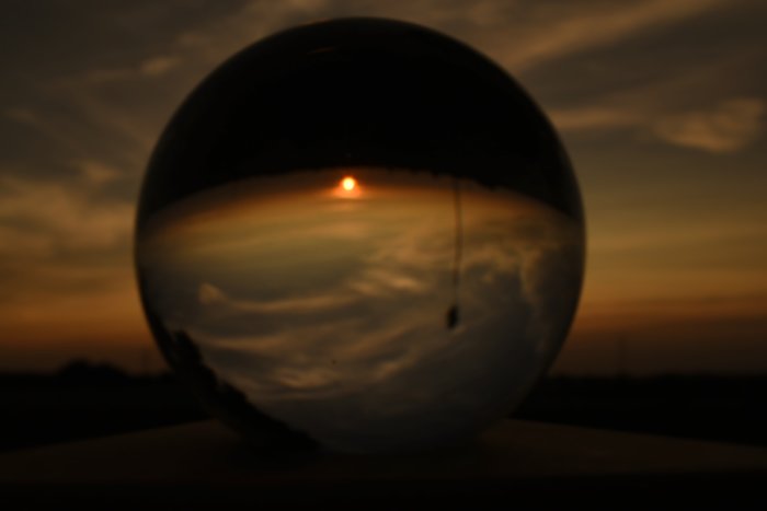 Solnedgång reflekterad i en kristallkula mot en mörknande himmel.