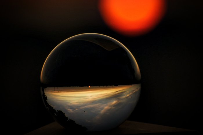 Kristallkula reflekterar omvänd landskapsvy vid solnedgång med suddig röd sol i bakgrunden.