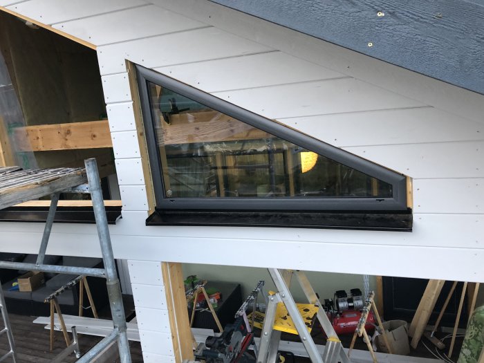 Takarbete med nyinstallerat gavelfönster på ett hus under konstruktion, verktyg i förgrunden.