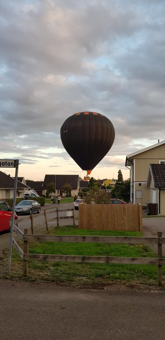 En varmluftsballong nära landning över ett bostadsområde vid skymning.