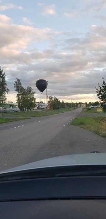 Varmluftsballong svävar nära vägen mot en molnig himmel vid skymningen.