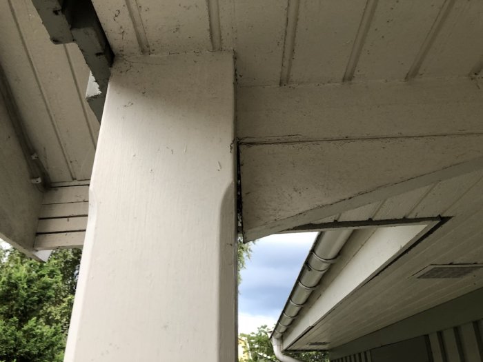 En synlig glipa mellan en vit pelare och taket på en entrétrapp där hängrännan och panelen visar tecken på skador och misspassningar.