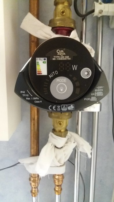Sammansatt cirkulationspump med märkningen Curacua, energiklass A, installerad på kopparledningar med vit trasa lindad runt en koppling.