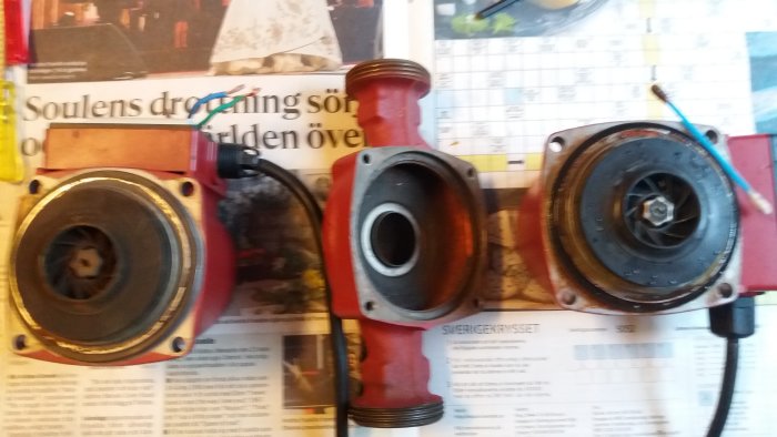 Delar av en pump med rött pumphus och synliga inre komponenter mot en tidningssida.