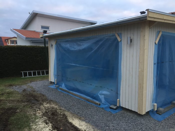 Byggnation av garage med uppsatt byggplast som väderskydd och grundmålad panel på väggarna.