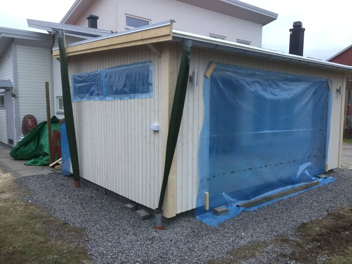 Garage under konstruktion med isolering, grundmålad panel och byggplast som väderskydd.