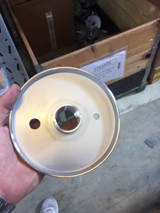 Hand håller en plan täckbricka med cirkulär form och centralt hål, i en butiksmiljö.