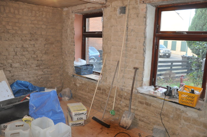 Renoveringsprojekt i vardagsrum med exponerade murade väggar och byggmaterial spridda på golvet.