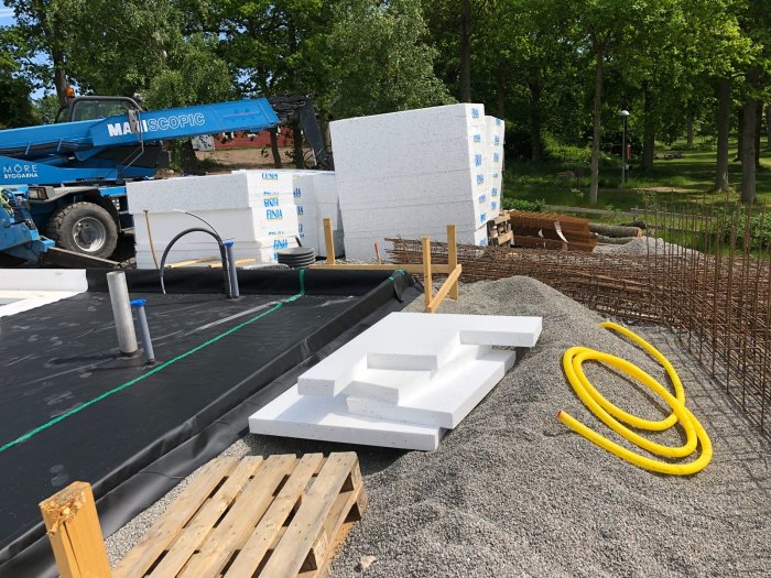 Byggarbetsplats med svetsade rör för köksö och kamin, byggmaterial och byggmaskiner i bakgrunden.