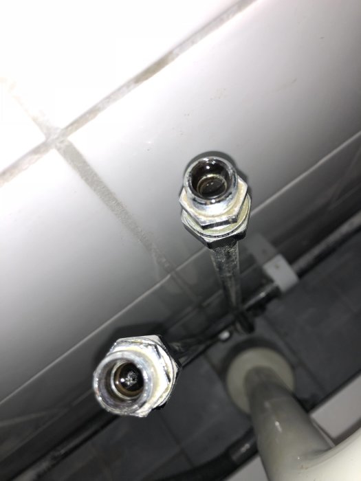 Närbild av otillpassade rördelar och anslutningsladden till en blandare mot kakelvägg.