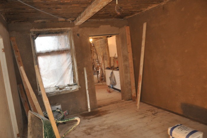 Renoveringsrum med nyapplicerad kalkgrund, öppet dörrhål, och byggmaterial på golvet.