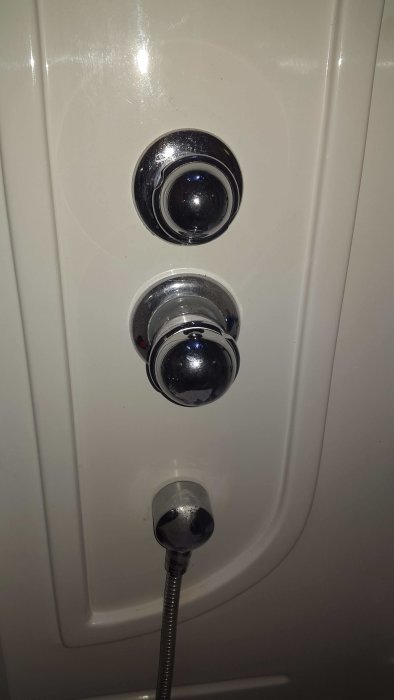 Framsida av duschkabinens blandare med över- och underrattar och duschslangens anslutning.